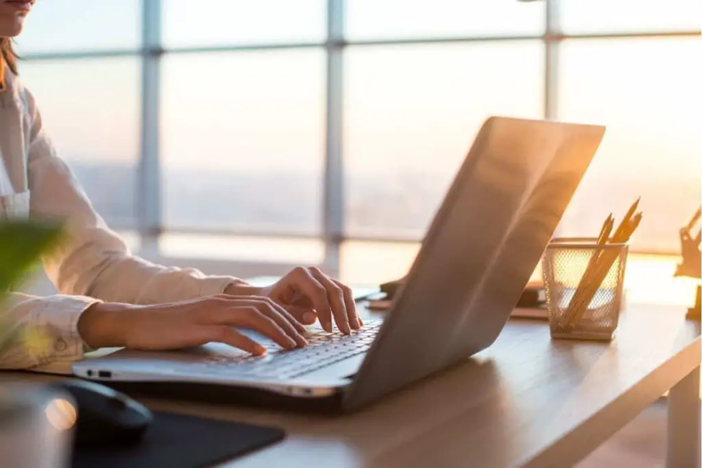 woman using a laptop on a table beside a window with golden sunlight coming in