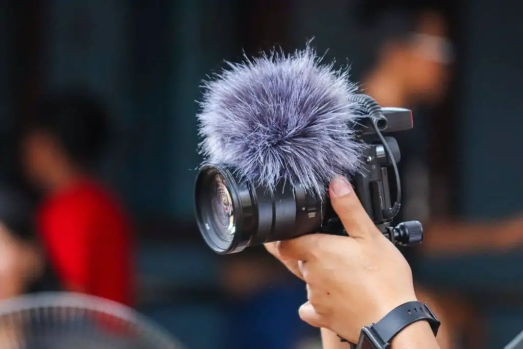 hands holding up a camera with a fluffy microphone on top of it