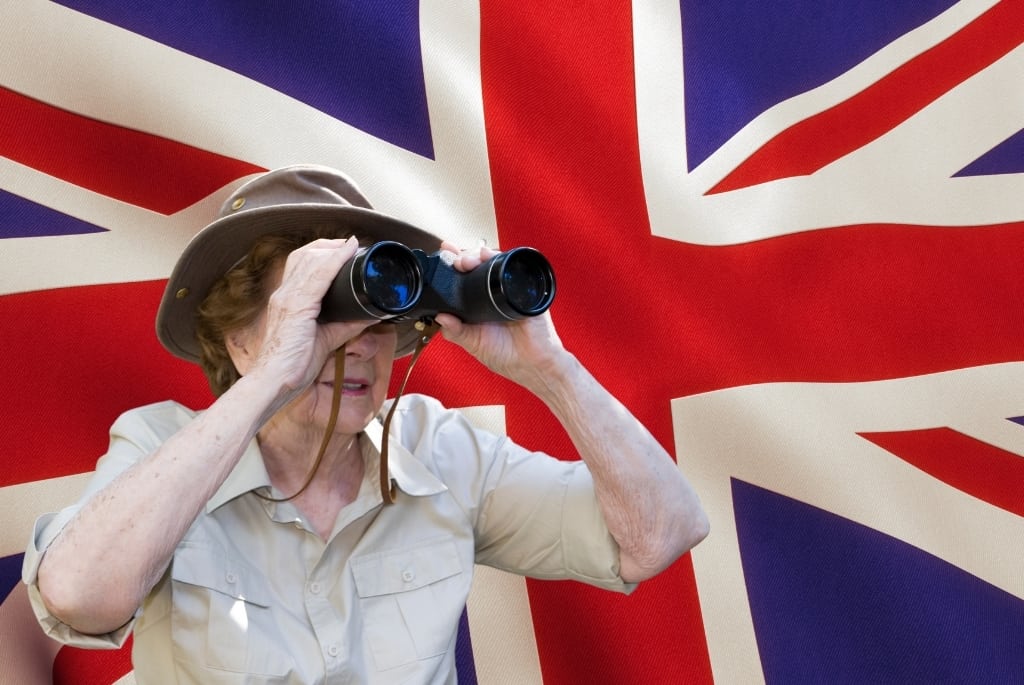 an elderly woman using binoculars while standing in front of a British flag
