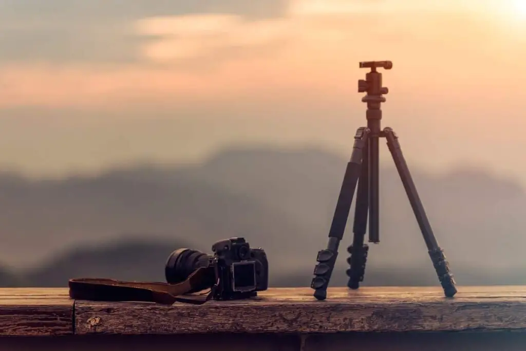 a tripod and dslr camera on a wooden railing at sunset