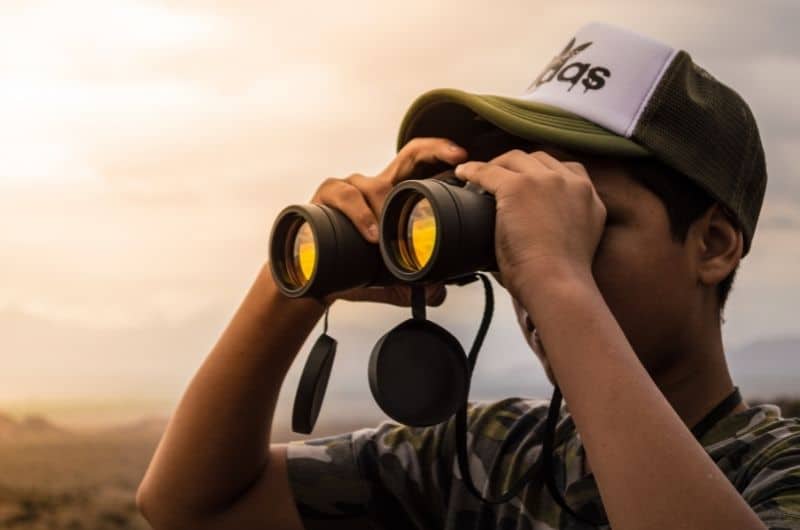 a teenage boy wearing a cap using binoculars to bird watch