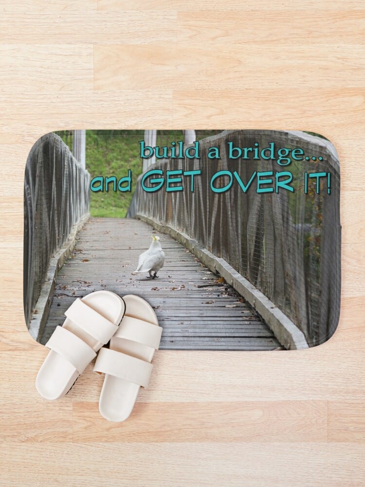 an overhead view of a bath mat with a cockatoo crossing a bridge and 'build a bridge...and get over it' printed on it. 