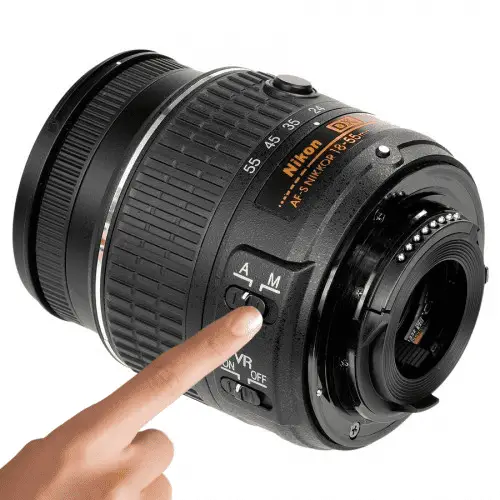 a Nikon 18-55mm lens with a woman's hand pressing the A/M focus switch