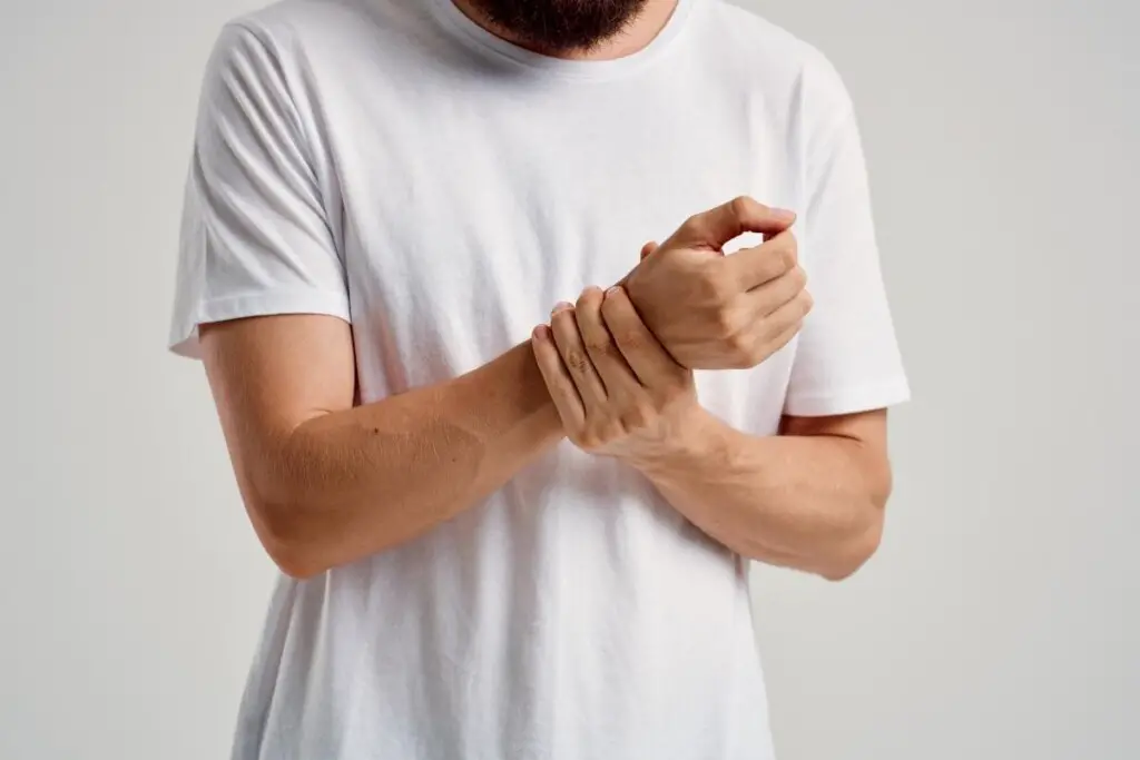 a man in a white t-shirt gripping his right wrist with his left hand