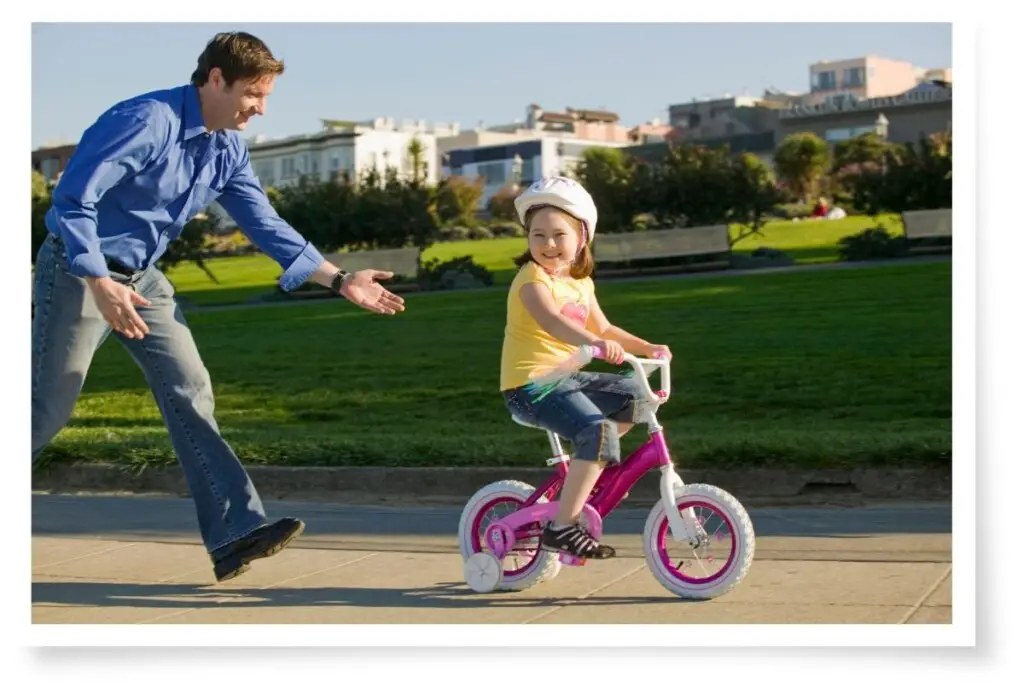 a father running after his daughter on her bicycle after he has just pushed her.