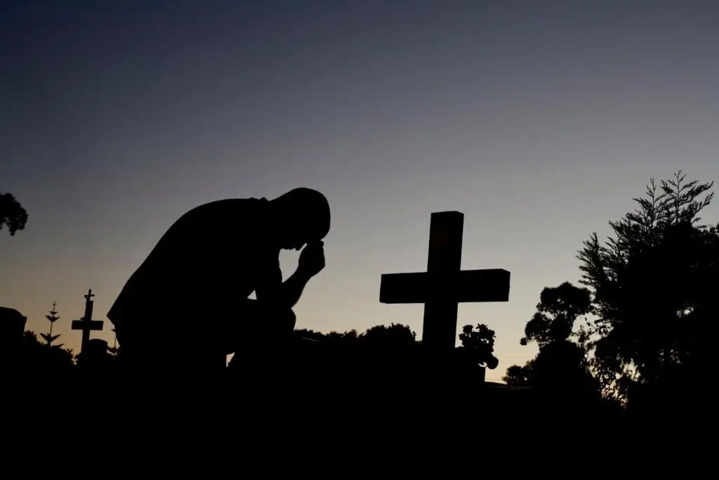 a silhouette of a man kneeling at a grave in a cemetary
