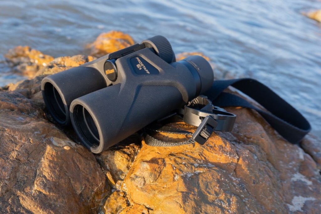 a pair of nikon prostaff 3S binoculars on a rock with water in the background