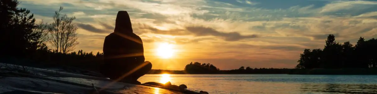 a person meditating by a lake at sunrise