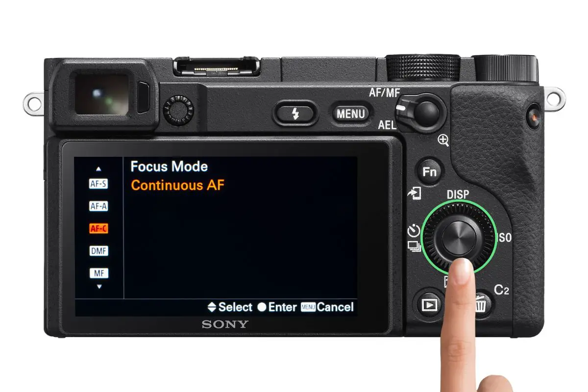 the rear of a Sony a6400 camera showing the Focus Mode screen with a woman's hand pressing the control wheel