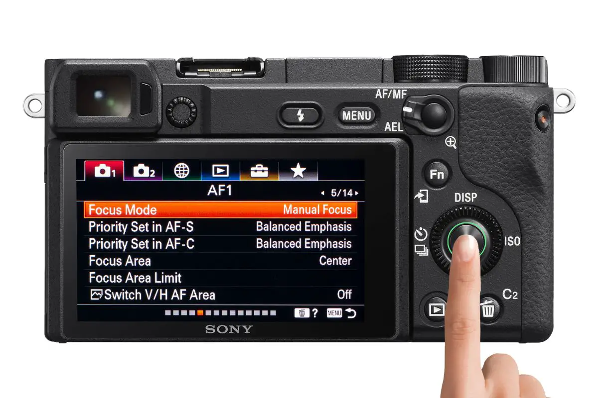 the rear of a Sony a6400 camera showing the Focus Mode menu with a woman's hand pressing the center button