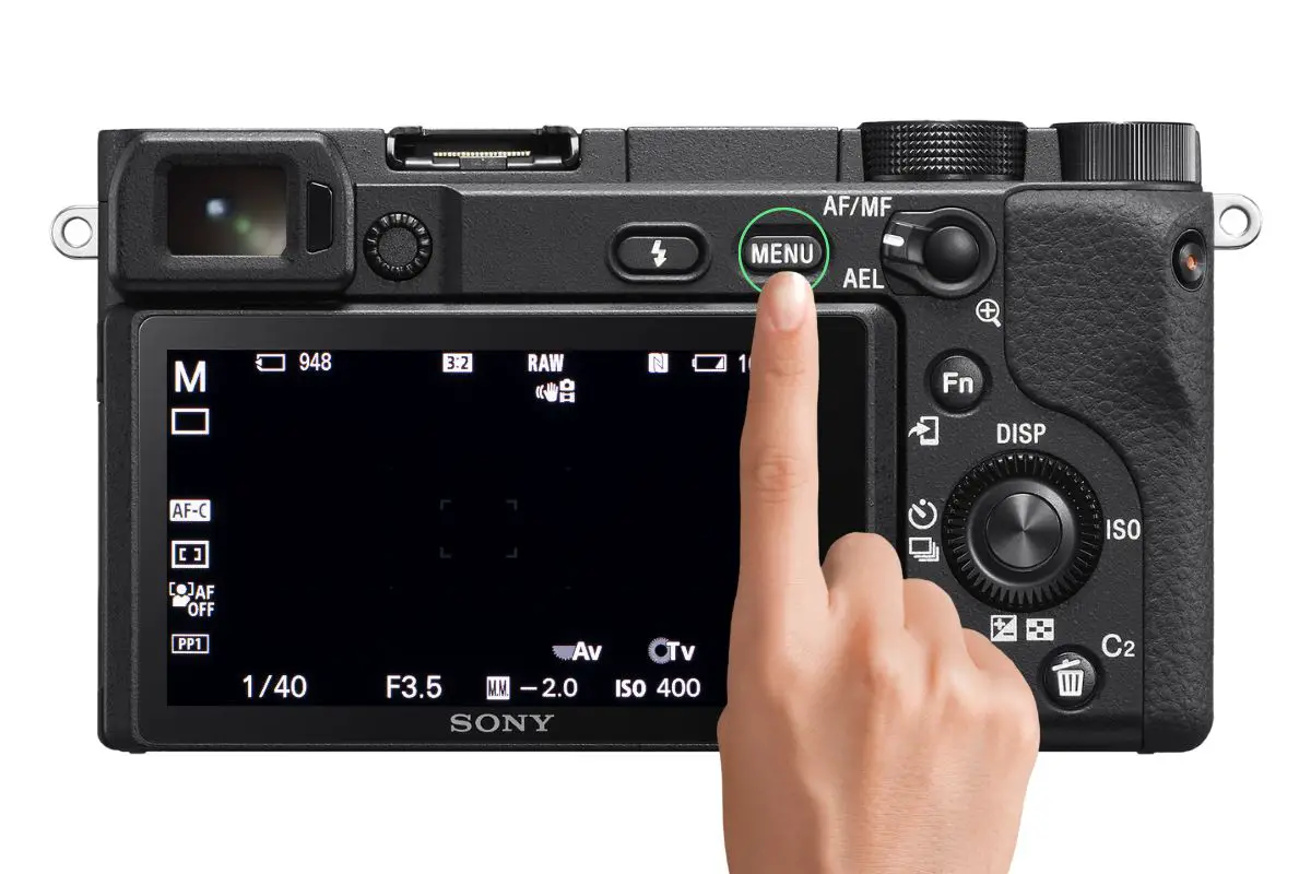 the rear of a Sony a6400 camera with a woman's hand reaching for the Menu button