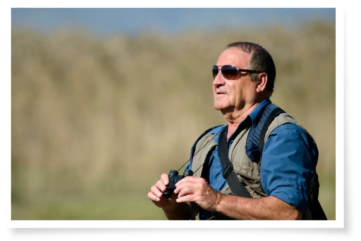 a man bird watching wearing sunglasses and a vest