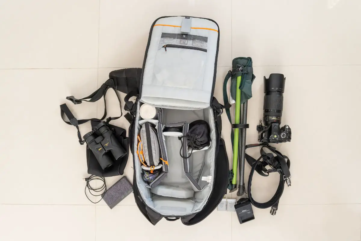 a photography backpack and camera gear laid out on a tile floor